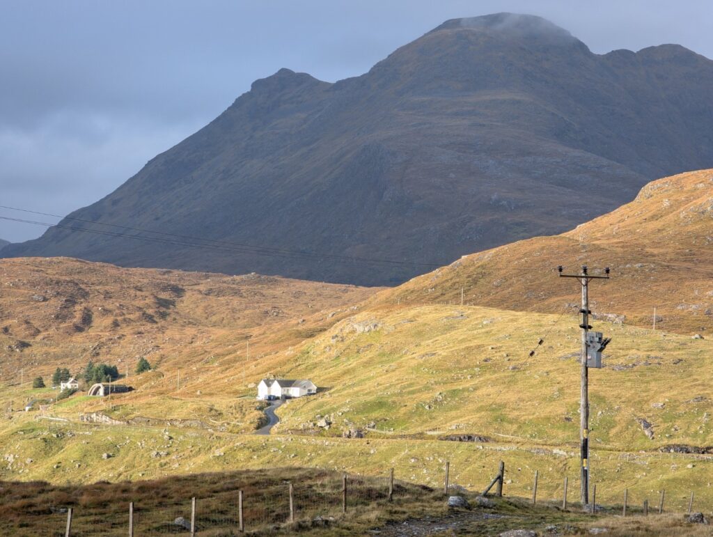 A lone power pole lower right is dwarfed by the rugged bare mountain in background.