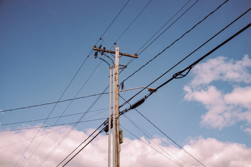 Dual use power/telephone pole with multiple cables in three directions. Blue sky behind. Credit: Conor Cook