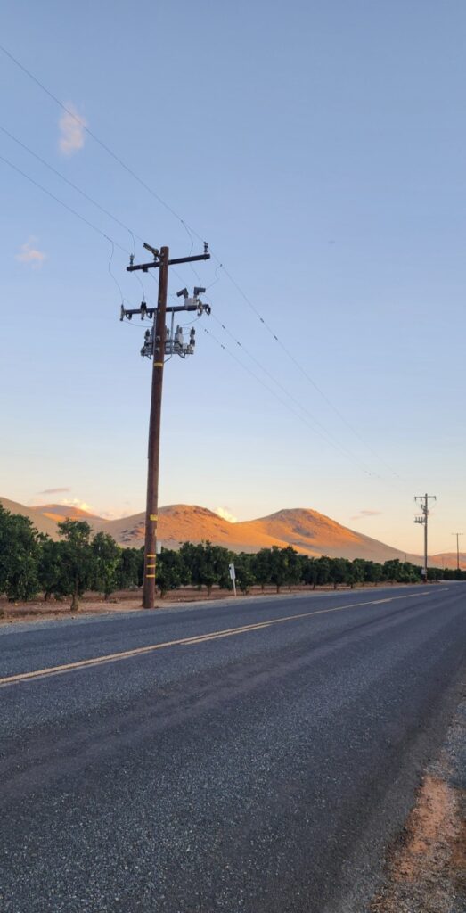 Power pole at sunset on side of main road with golden sunlit hills in background